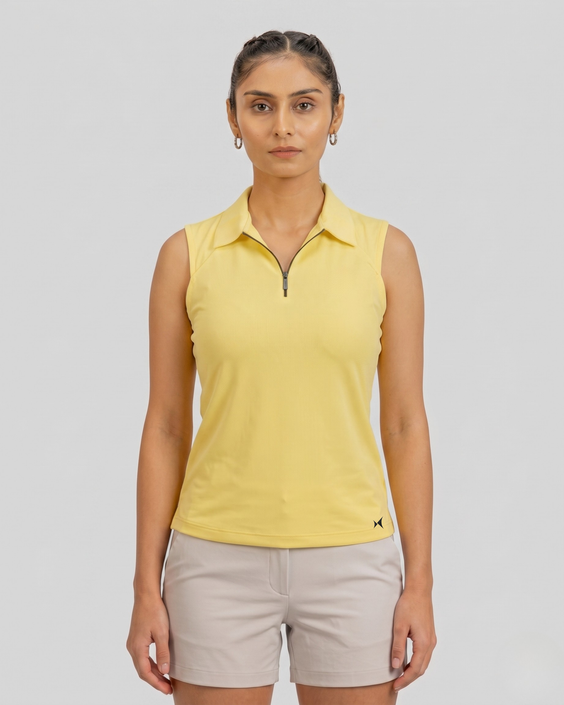 Woman wearing a yellow sleeveless polo shirt and beige shorts on a gray background