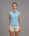 Woman wearing a light blue sleeveless polo shirt and beige shorts on a gray background