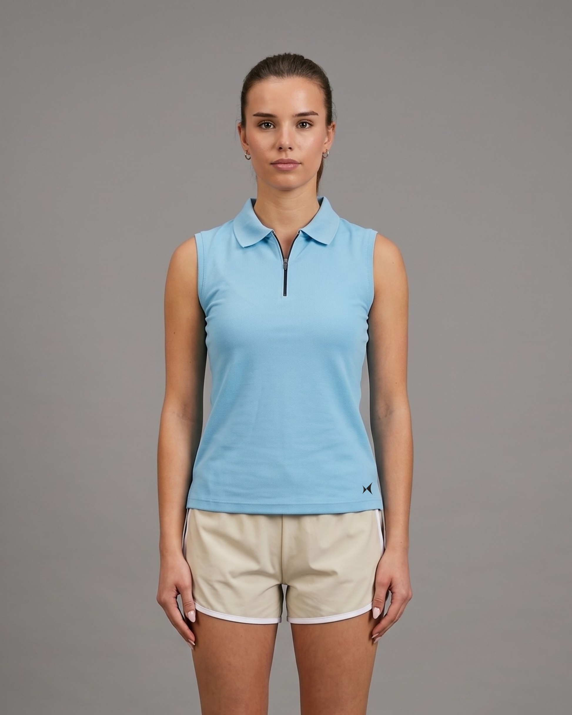 Woman wearing a light blue sleeveless polo shirt and beige shorts on a gray background