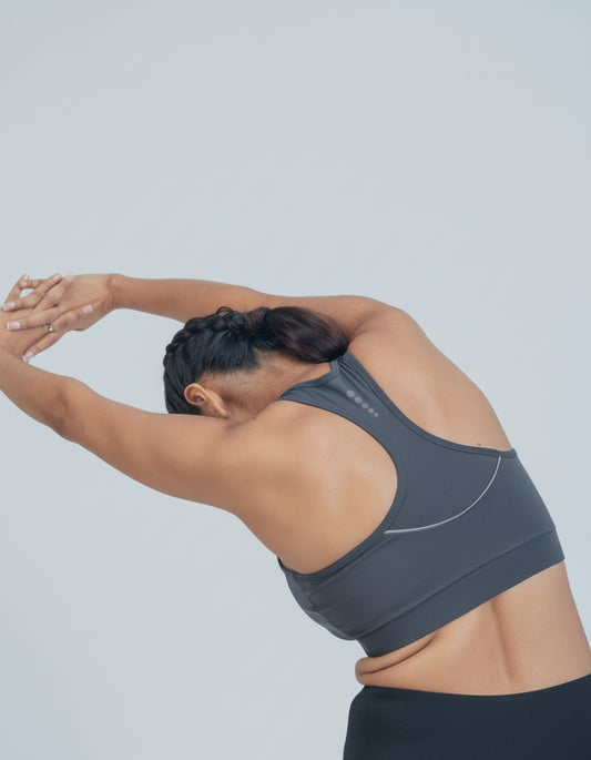 Person wearing a gray sports bra stretching against a light gray background