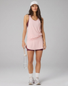 Woman wearing a pink athletic dress and white sneakers on a gray background