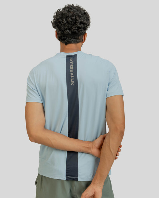 Person wearing a light blue t-shirt with a dark gray stripe on the back, standing against a plain background.