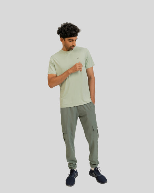 Man wearing a light green t-shirt and cargo pants on a plain background