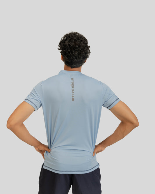 Person wearing a light blue t-shirt with a brand logo on the back against a gray background