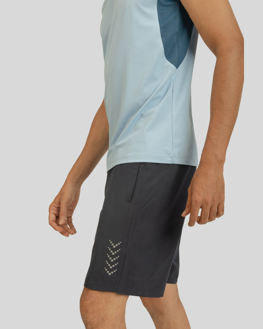 Person wearing a light blue sleeveless shirt and black shorts with a logo on a plain background