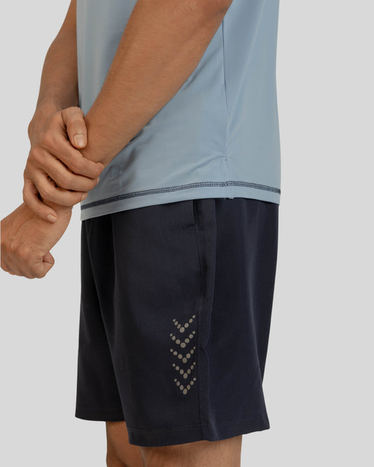 Person wearing a light blue shirt and dark shorts on a plain background