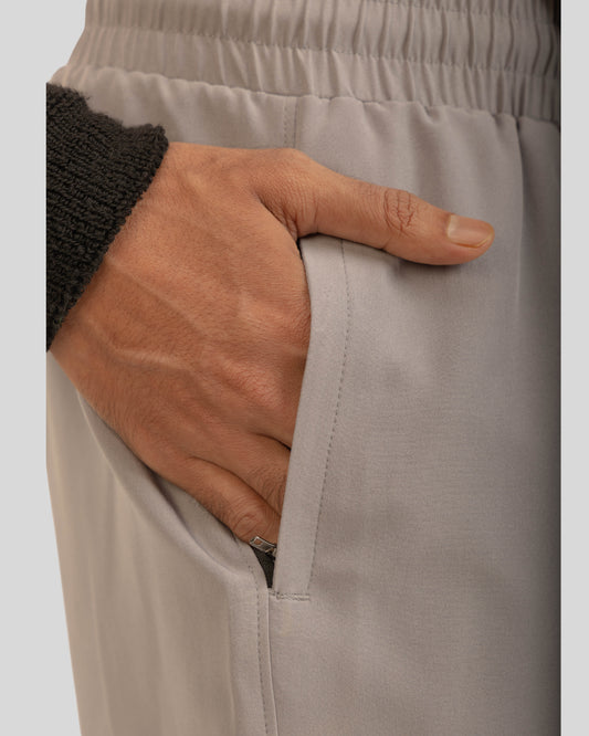 Close-up of a hand adjusting beige pants on a plain background