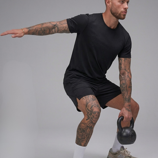 Man in black t-shirt and shorts holding a kettlebell against a gray background