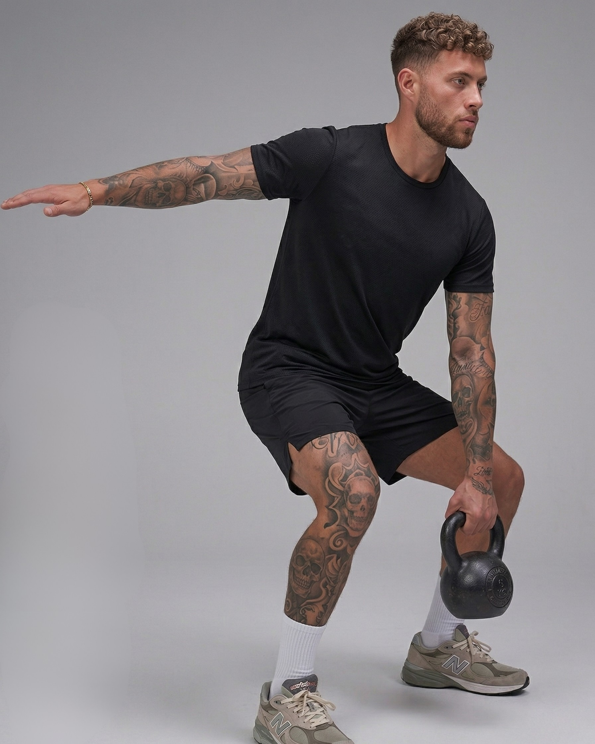 Man in black t-shirt and shorts holding a kettlebell against a gray background