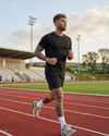 Man running on a track with stadium seats and greenery in the background