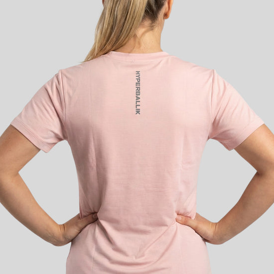 Person wearing a pink t-shirt with a brand logo on the back against a gray background