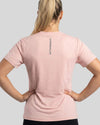 Person wearing a pink t-shirt with a brand logo on the back against a gray background