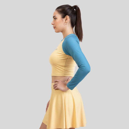 Woman wearing a yellow dress with a blue long-sleeve top on a gray background