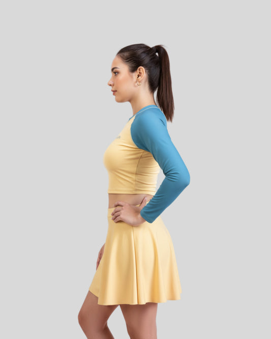 Woman wearing a yellow dress with a blue long-sleeve top on a gray background