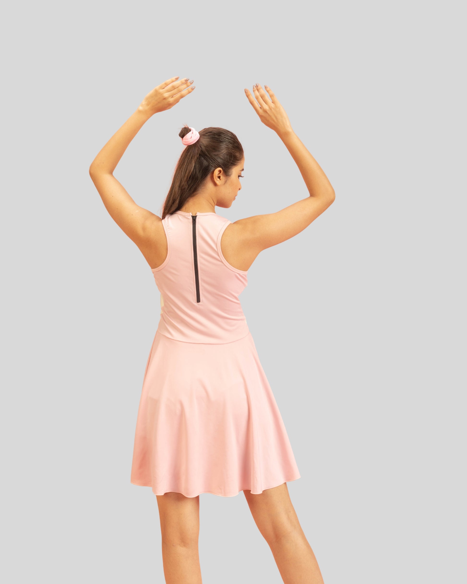 Woman wearing a pink dress with her arms raised on a gray background