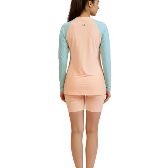 Woman wearing a peach long-sleeve shirt and light blue shorts on a white background