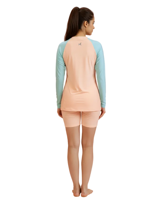 Woman wearing a peach long-sleeve shirt and light blue shorts on a white background