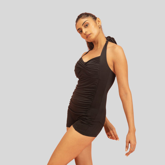 Woman wearing a black one-shoulder swimsuit on a light gray background
