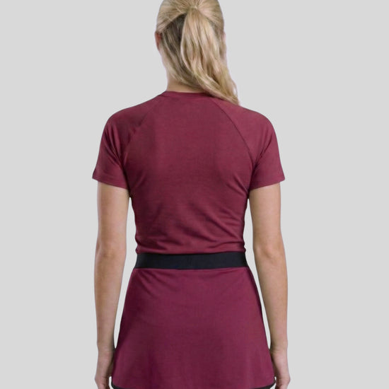 Person wearing a maroon athletic outfit with a skirt on a plain background