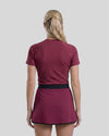 Person wearing a maroon athletic outfit with a skirt on a plain background