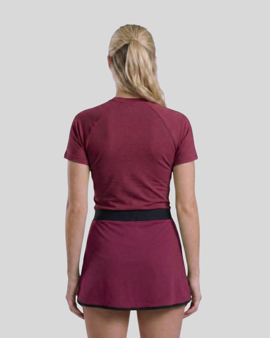 Person wearing a maroon athletic outfit with a skirt on a plain background