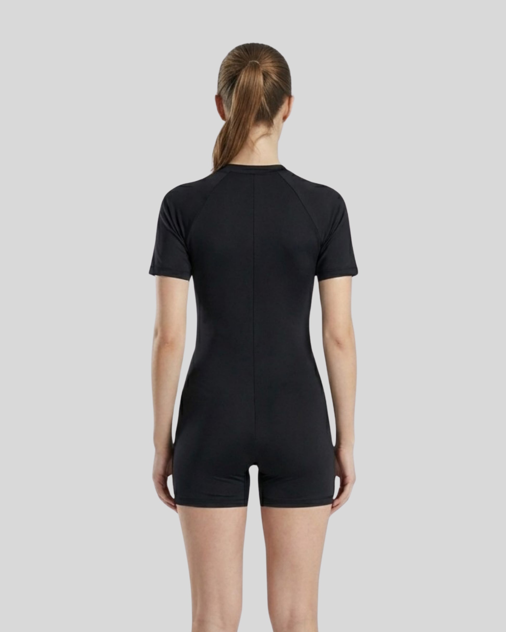 Person wearing a black bodysuit against a light gray background