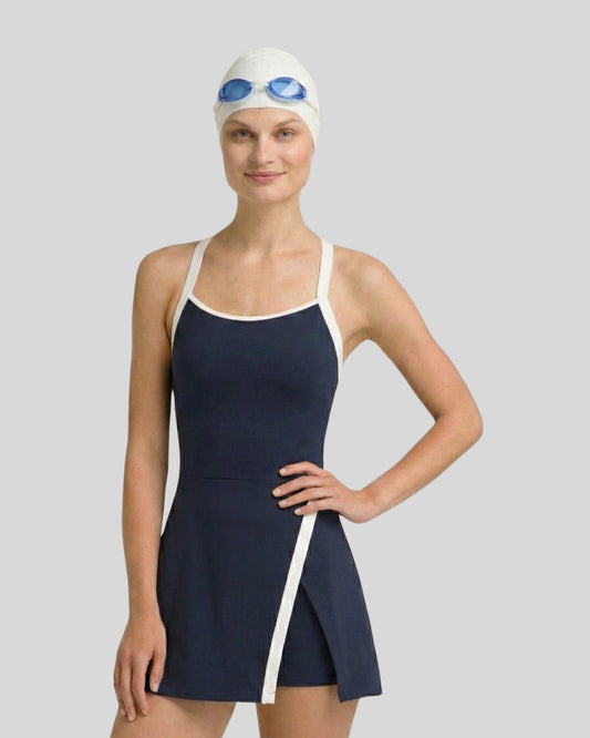 Woman wearing a navy swimsuit with white trim, white swim cap, and blue goggles on a gray background