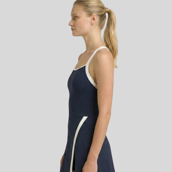 Woman wearing a navy swimsuit with white accents on a plain background
