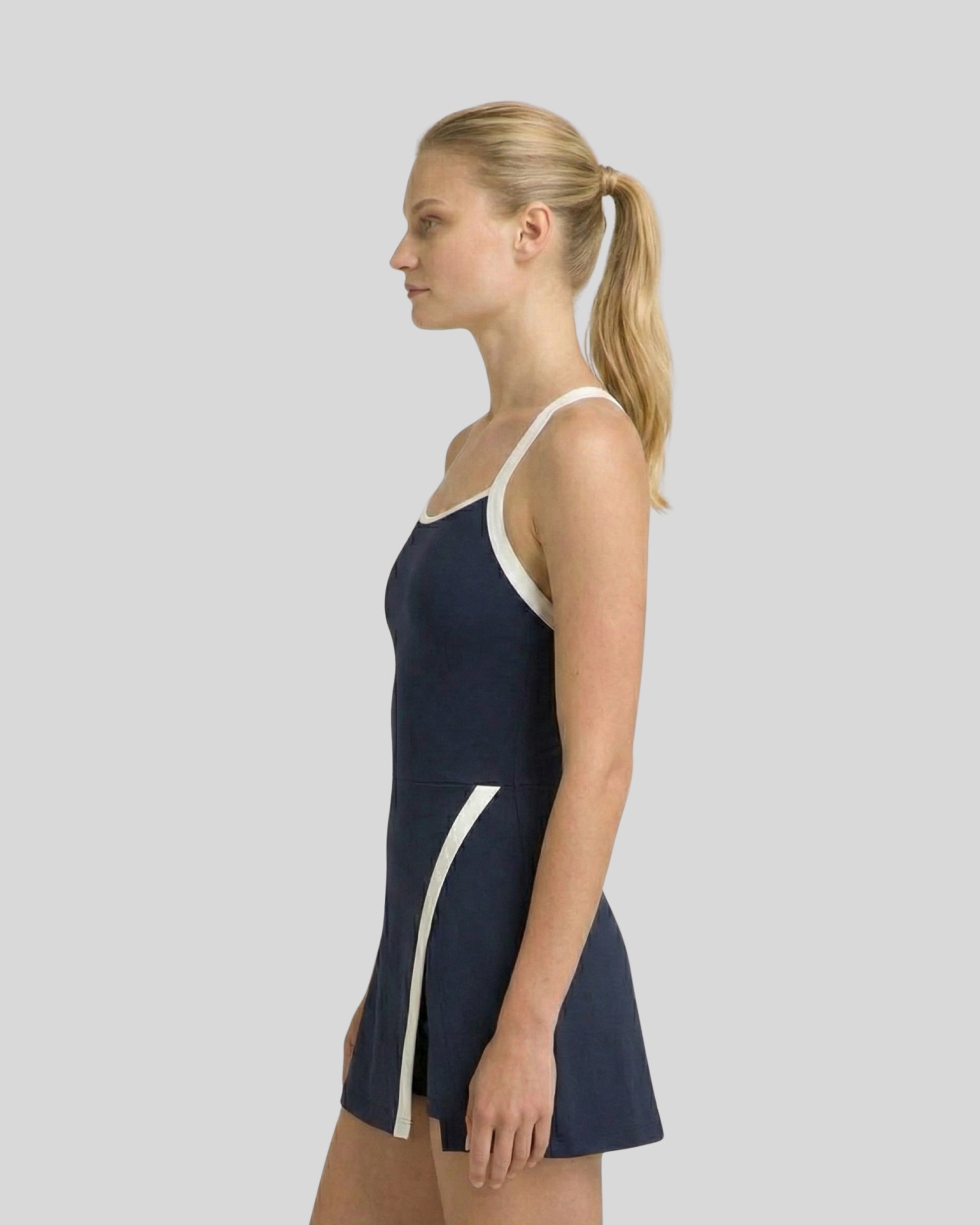 Woman wearing a navy swimsuit with white accents on a plain background