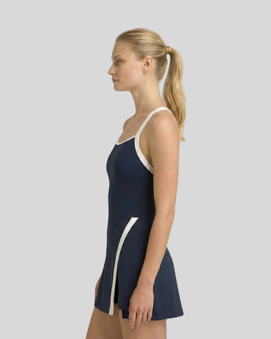 Woman wearing a navy swimsuit with white accents on a plain background