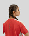 Person wearing a red and white sports jersey with a logo on the back against a light gray background