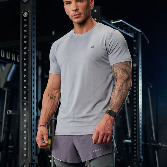 Man wearing a gray athletic outfit with visible tattoos in a gym setting