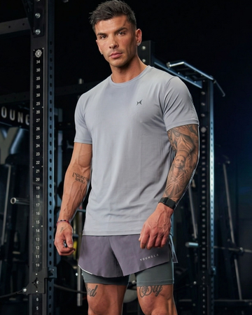 Man wearing a gray athletic outfit with visible tattoos in a gym setting