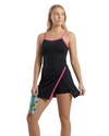 Woman wearing a black and pink athletic dress holding goggles on a white background