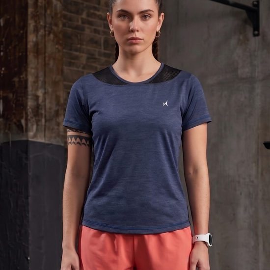 Woman wearing a blue athletic shirt and pink shorts against a brick wall.