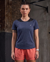 Woman wearing a blue athletic shirt and pink shorts against a brick wall.