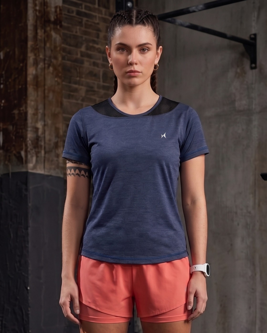 Woman wearing a blue athletic shirt and pink shorts against a brick wall.