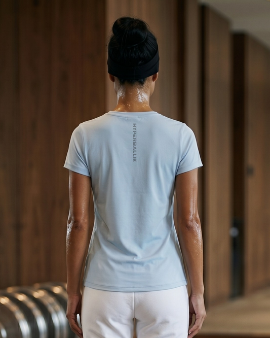 Person wearing a light blue t-shirt and white pants in a wooden interior setting