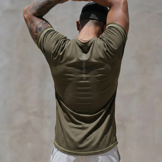 Person wearing an olive green athletic shirt and white pants against a neutral background