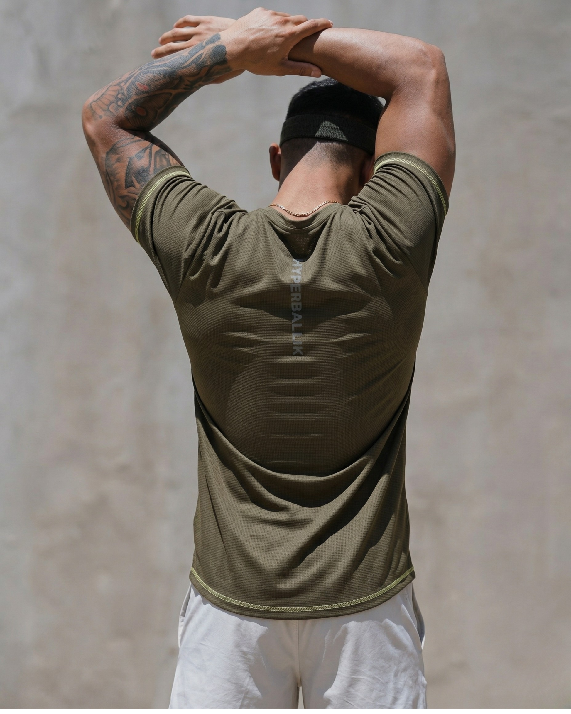 Person wearing an olive green athletic shirt and white pants against a neutral background