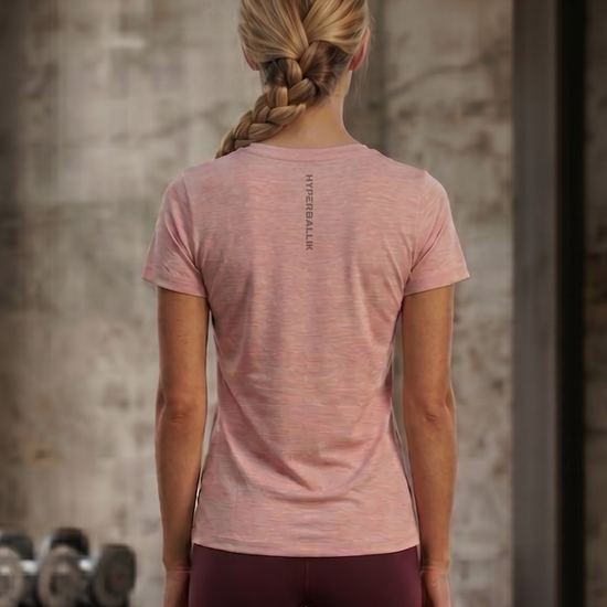 Person wearing a pink t-shirt with text on the back, standing in a gym setting.