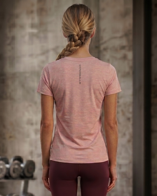 Person wearing a pink t-shirt with text on the back, standing in a gym setting.