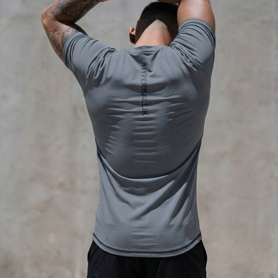 Person wearing a gray athletic shirt with 'HYPERJOCK' branding, stretching outdoors.