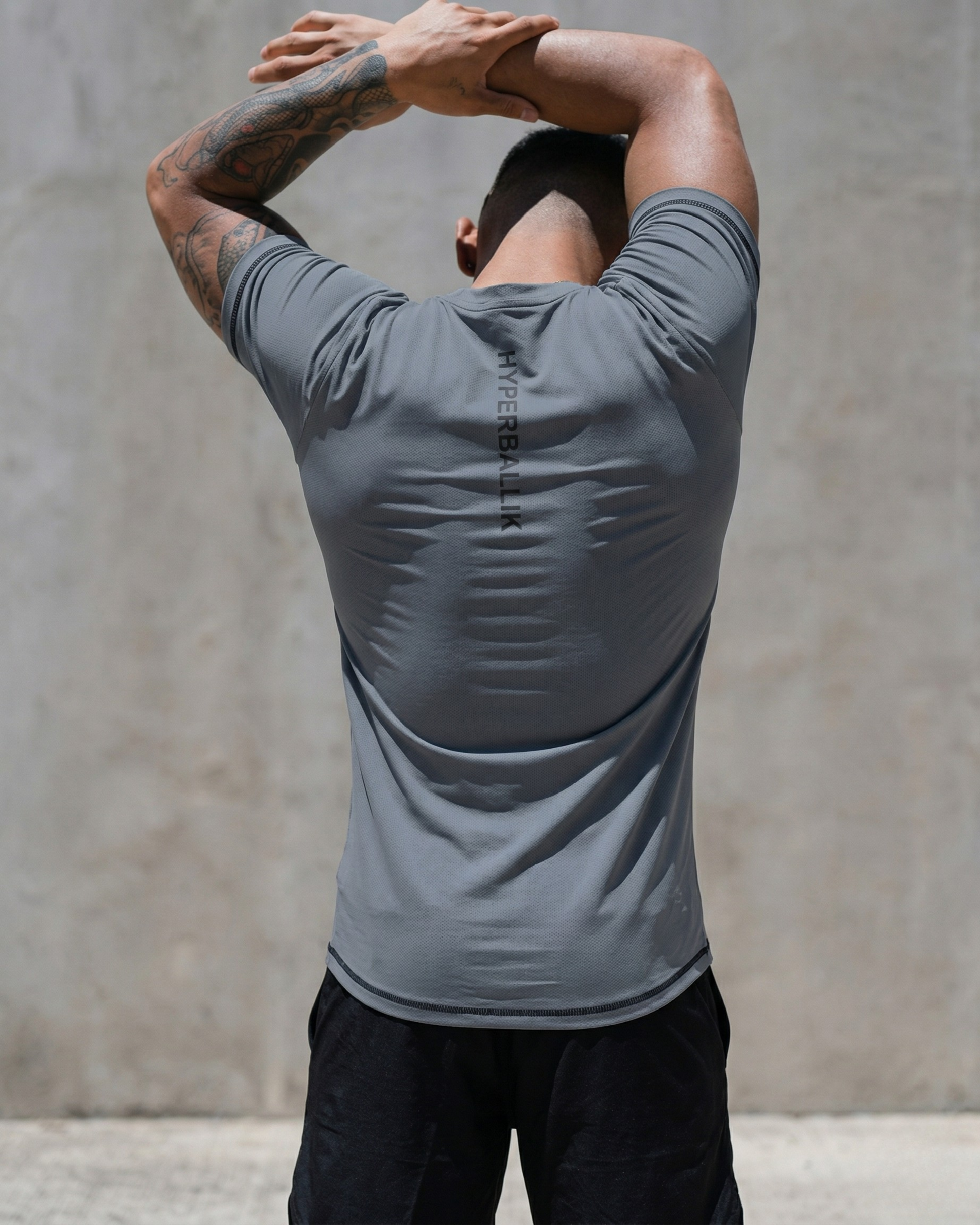 Person wearing a gray athletic shirt with 'HYPERJOCK' branding, stretching outdoors.