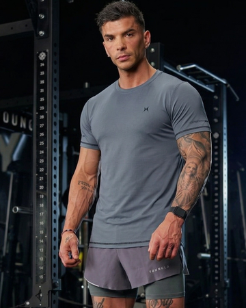 Man wearing a gray athletic outfit with tattoos on his arms and legs, standing in a gym setting.