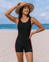 Woman wearing a black swimsuit with pink trim on a beach