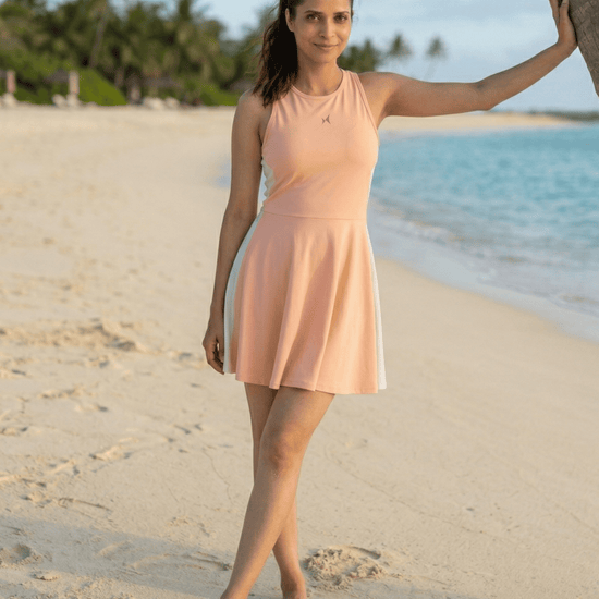 Woman in a peach dress standing on a sandy beach with palm trees and water in the background