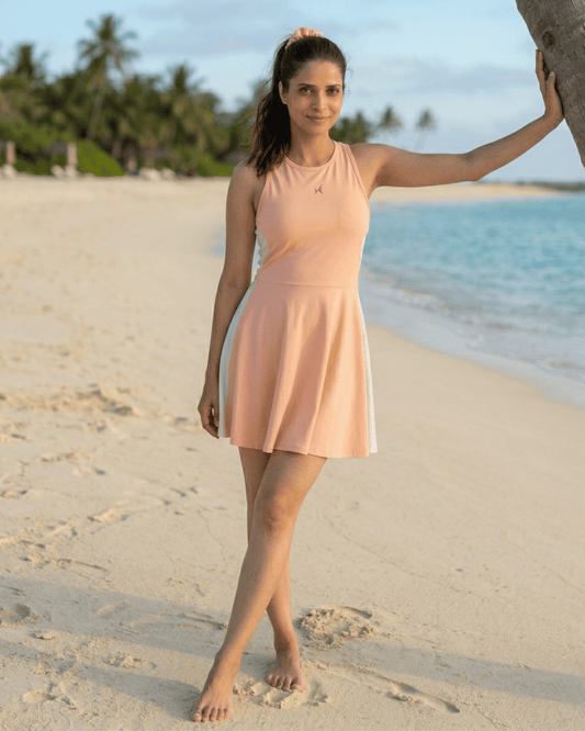 Woman in a peach dress standing on a sandy beach with palm trees and water in the background