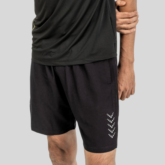 Person wearing black athletic shorts with a logo on a plain background