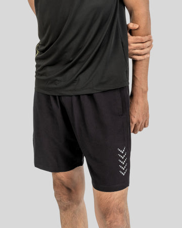 Person wearing black athletic shorts with a logo on a plain background